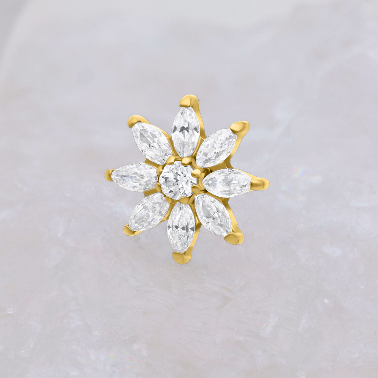 Goldener Piercing Aufsatz in Blütenform mit klaren Kristallen auf hellem Hintergrund